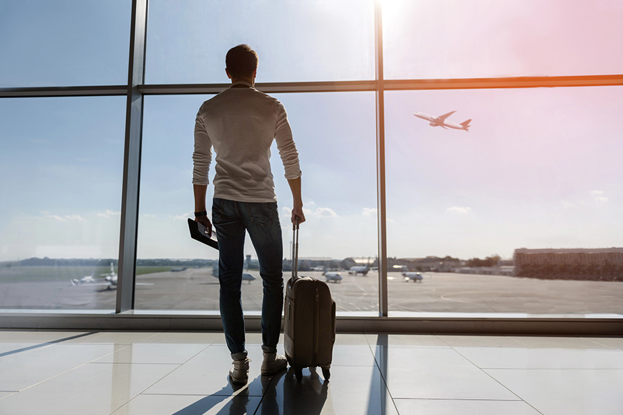 A person with a suitcase at an airport watching a plane, highlighting the benefits of traveling for rehab