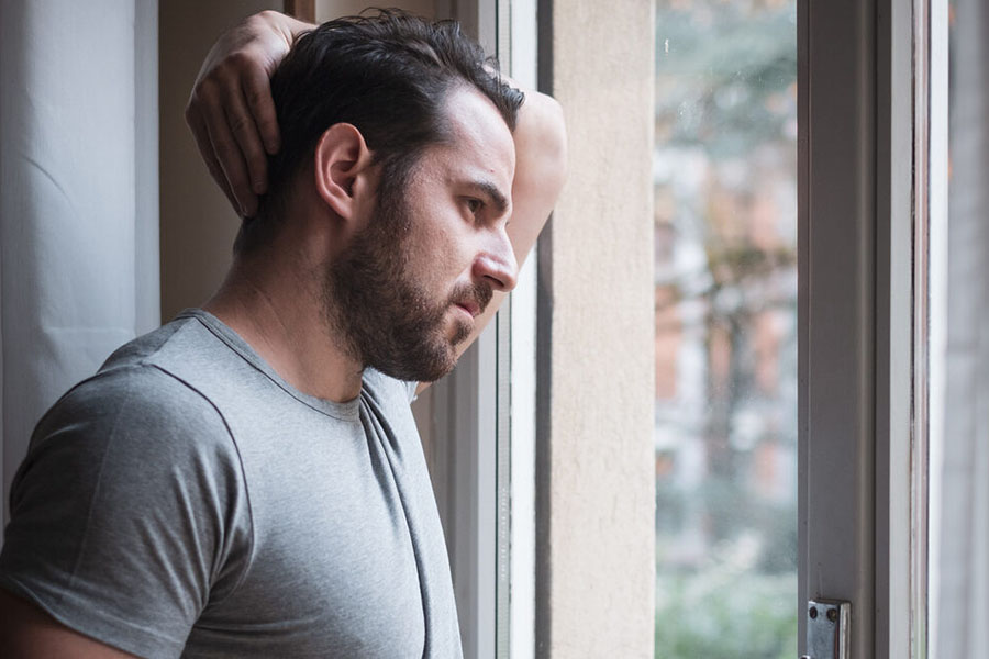 Adult male looking out the window while holding his head suffering from one of the most common co-occurring disorders