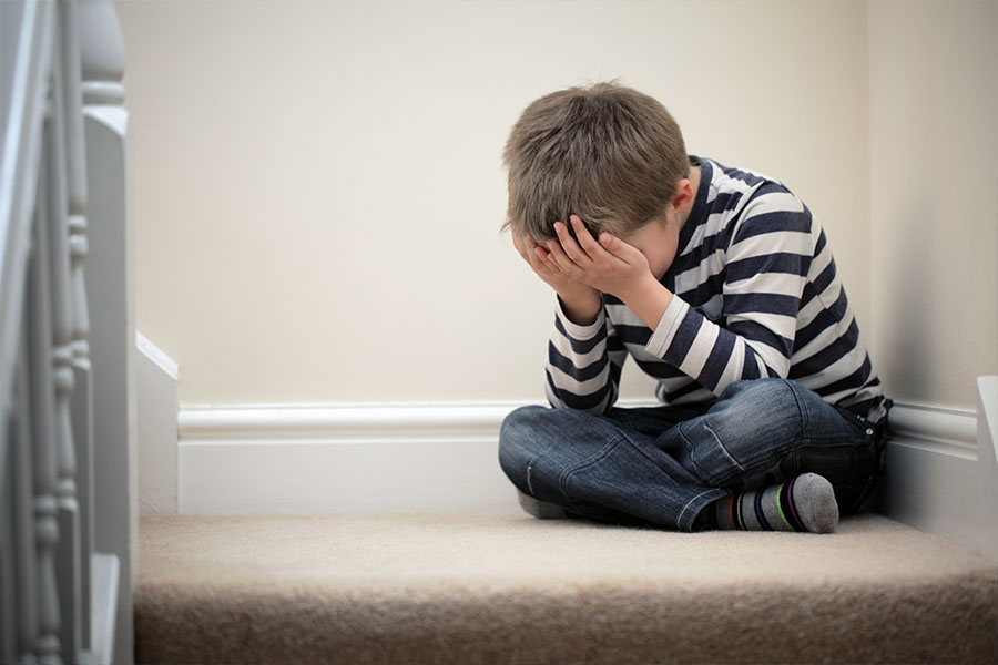 Child sitting in the corner with hands covering his face concept image for childhood trauma and mental health