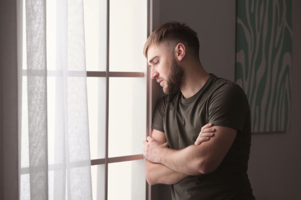 Depressed young man looking out the window concept image for psychological impact
