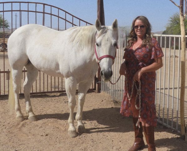 Equine therapist standing with a white rescue horse in an outdoor pen