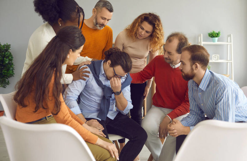 Recovery community consoling young man during the addiction treatment session. Recovery community centers serve as local resources of community-based recovery support. Some are non-profit and supported by Department of Mental Health and Substance Abuse Services.