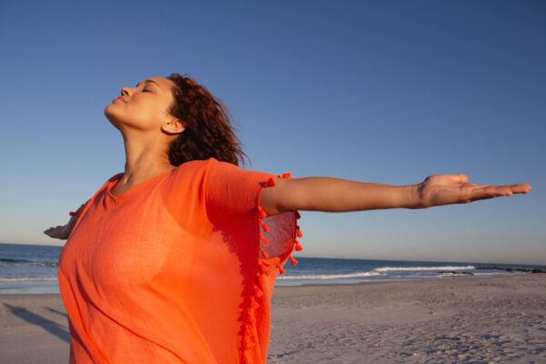 Woman standing on the beach with open arms, symbolizing freedom and balance found through holistic treatments