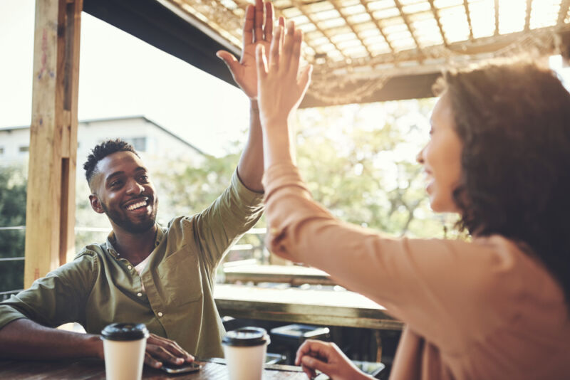 A smiling man and woman sharing a celebratory high five over coffee, reflecting the importance of aftercare in recovery