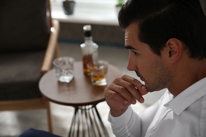 A man in deep thought sitting near a table with whiskey and glasses, representing signs of a high functioning alcoholic