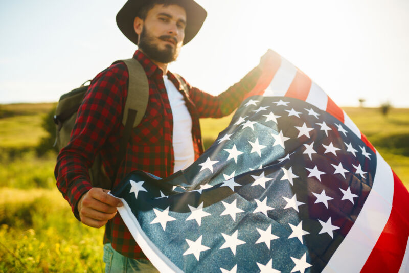 veteran rehab programs A bearded man in a hat holding an American flag outdoors, symbolizing recovery through veteran rehab programs